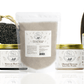 A variety of organic skincare essentials by Natural Elephant, including prickly pear seed oil, argan oil, henna powder, Moroccan black soap, and Ghassoul clay, alongside a pumice stone and exfoliating glove.